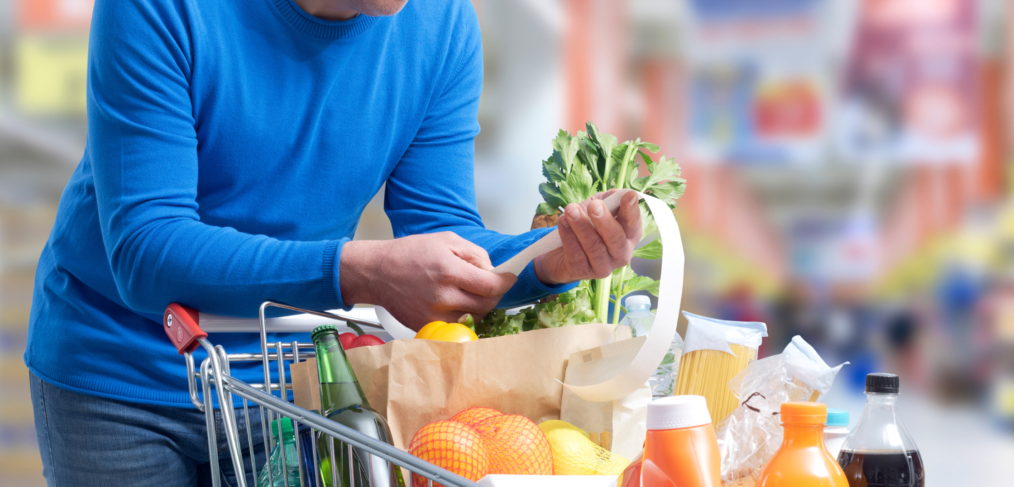 Canadian grocery shopper holding a small basket and checking prices on her phone in a grocery store aisle